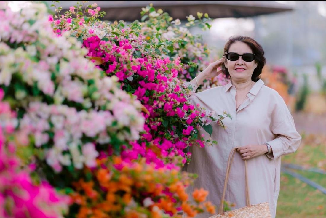 A senior woman in sunglasses beside a wall of pink bougainvillea